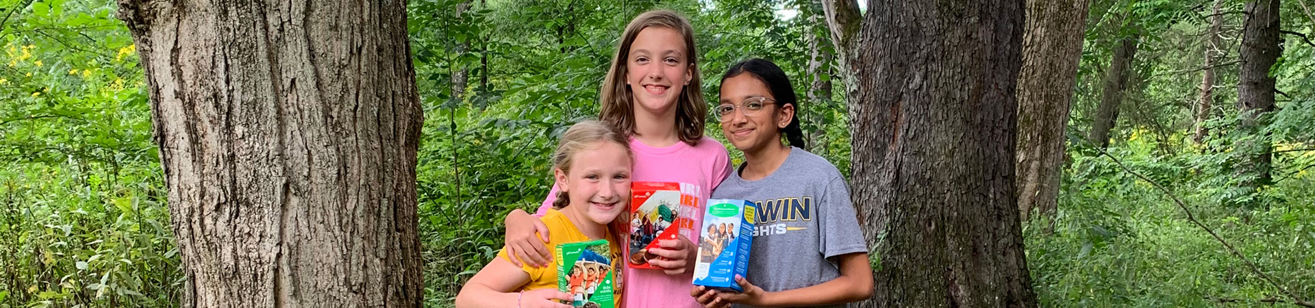  three girls holding cookie boxes and smiling 