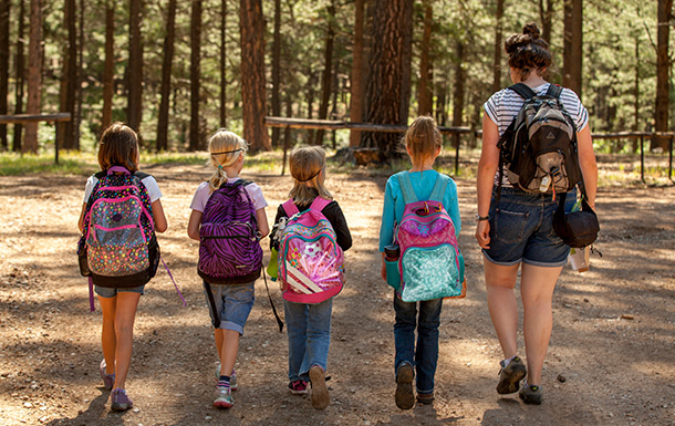 girls wearing backpacks walking with a camp counselor